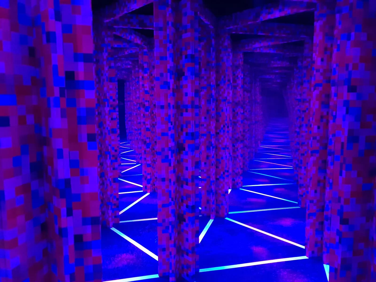 A long, dark corridor with walls made of textured purple, red, and blue blocks, illuminated by neon blue zigzag lines on the floor.